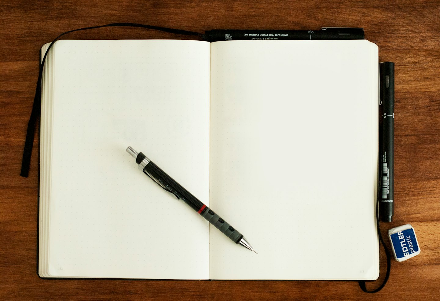 Blank notebook with pencil, pen, and eraser on a wooden table.